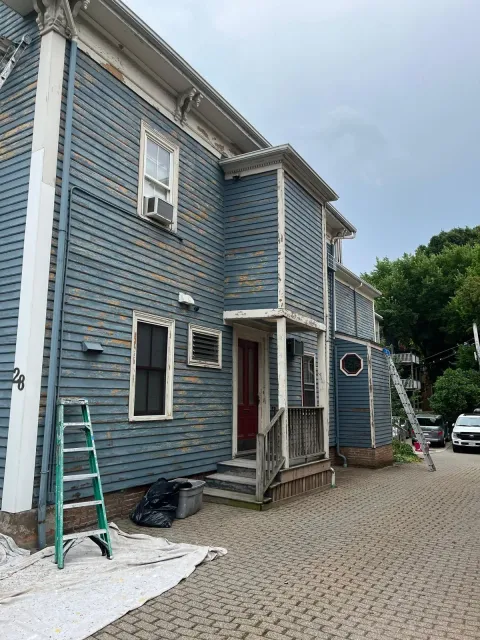 Blue two-story house with white trim, a front porch, ladder, and gravel driveway under construction.