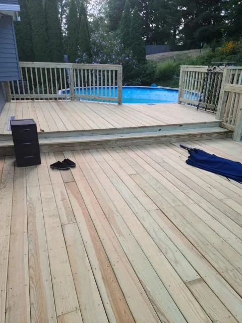 A wooden deck with a small gated area overlooking a backyard with a swimming pool surrounded by trees and bushes.