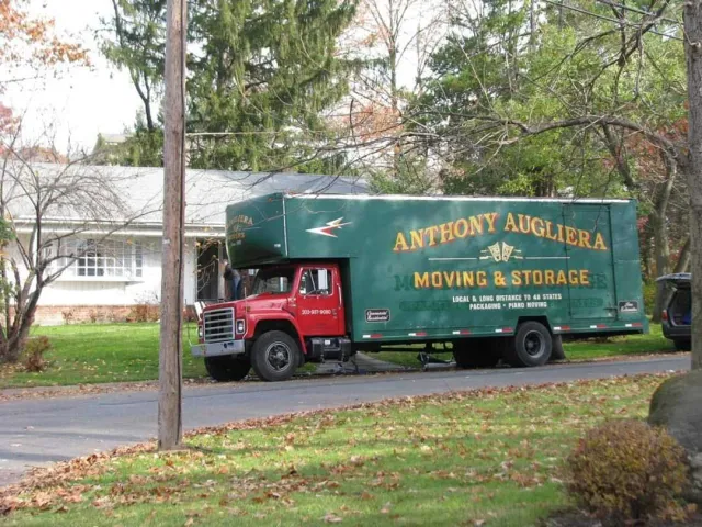 A green moving and storage truck is parked on the side of the road