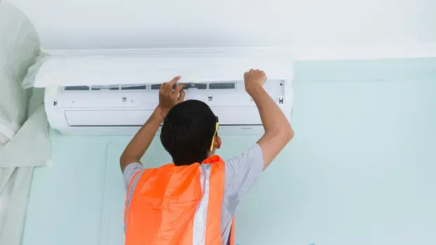 A man is installing an air conditioner on a wall.