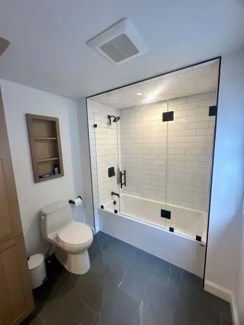 Bathroom with glass shower, white tub, black fixtures, and dark gray tile floor.