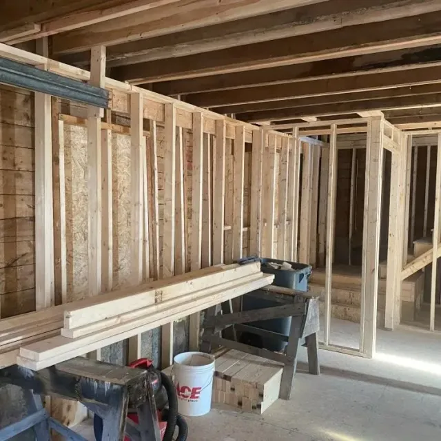 Unfinished basement with exposed wooden framing, stacked lumber, and construction tools.