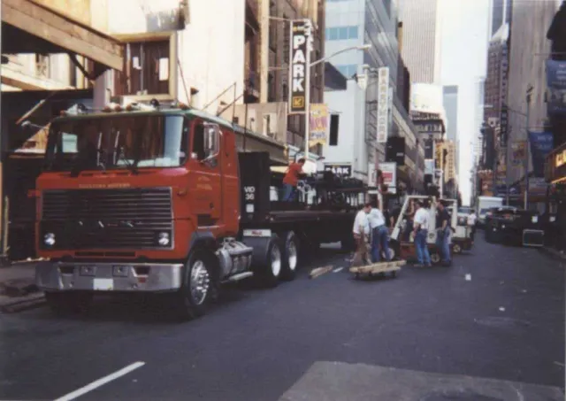 A large red truck is driving down a city street in front of a park sign