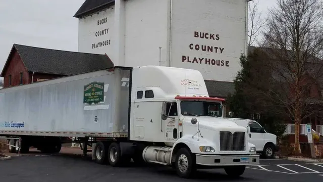 A white semi truck is parked in front of a building that says bucks county flat hobie.