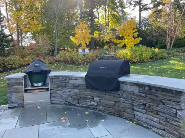 Outdoor kitchen installation in Marblehead MA with natural stone veneer wall and built-in grill on backyard patio.
