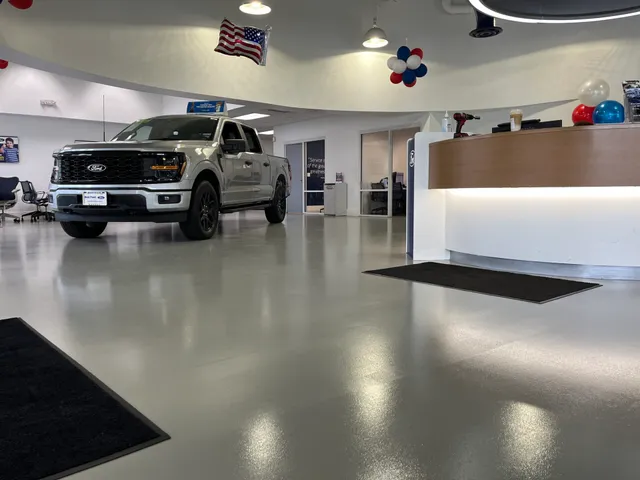The picture depicts a Ford car dealership show room with a gray epoxy floor.