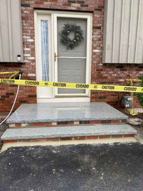 Front steps of a brick house with new gray granite treads and a yellow caution tape strung across the doorway.