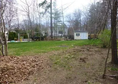 A large yard with a house in the background and trees in the foreground.