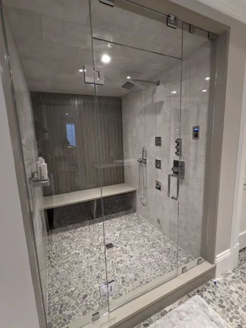Modern walk-in shower with glass enclosure, pebble floor, built-in bench, and multiple shower heads and controls.