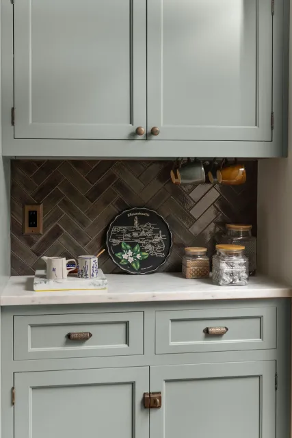 Mint green kitchen cabinets with a herringbone backsplash and countertop decor