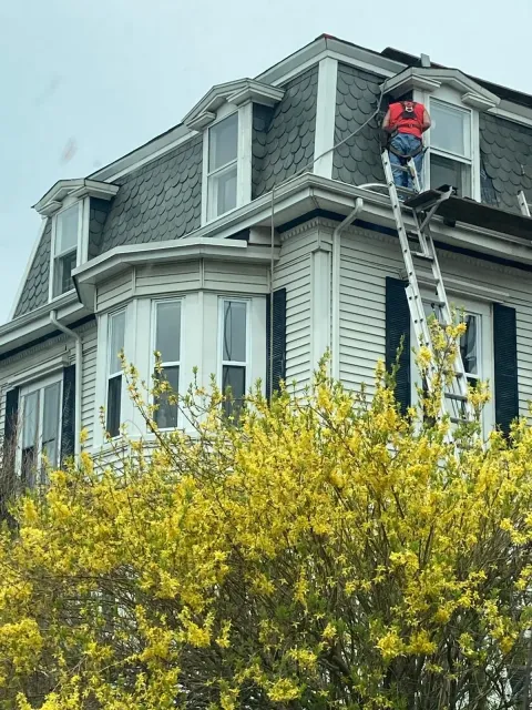 A man is standing on a ladder on the roof of a house.