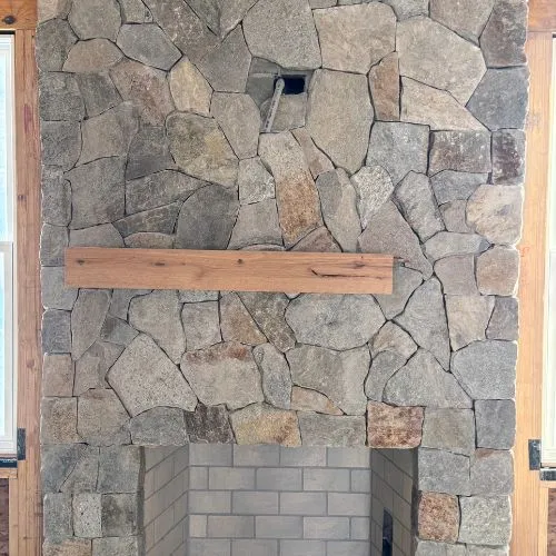 Stone fireplace with irregular gray rocks and wooden mantel shelf