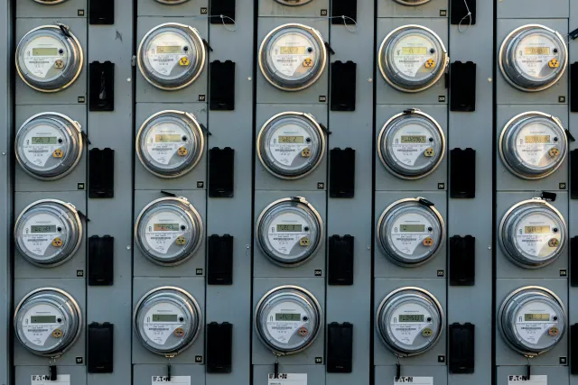 Multiple electric meters mounted on a gray panel, arranged in rows.