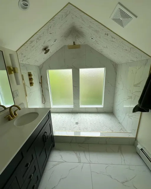 Bright bathroom with black vanity, white marble floor, and a sloped ceiling over a frosted window.