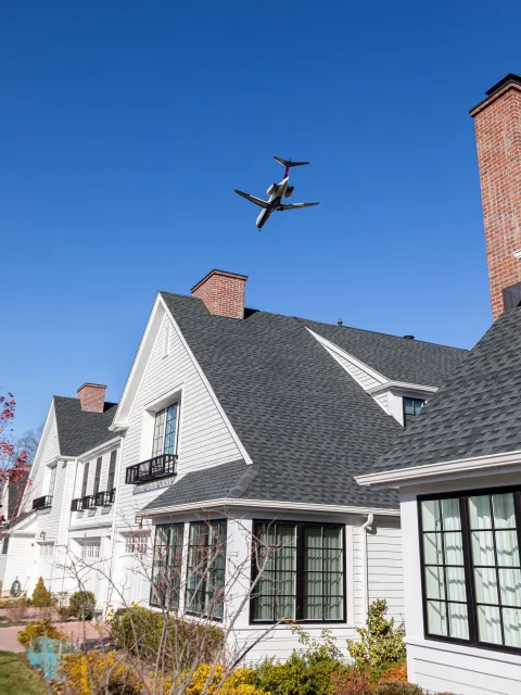 A plane is flying over a white house with a gray roof