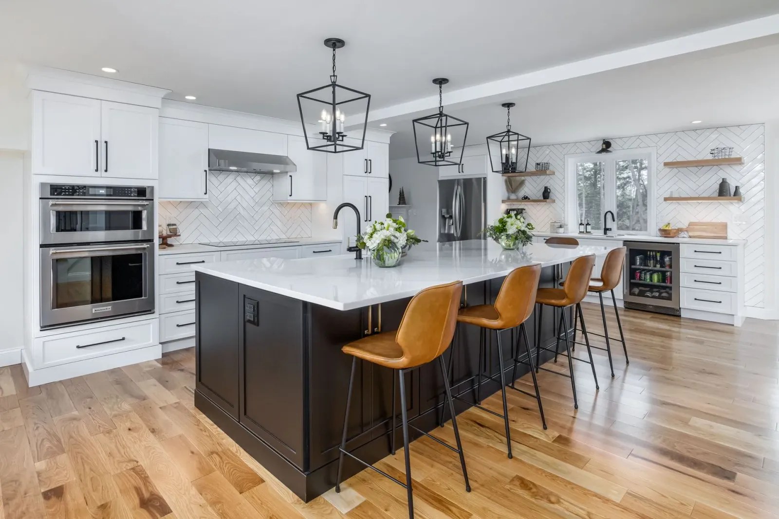 Bright modern kitchen with white cabinets, black island, and three tan barstools on hardwood floors
