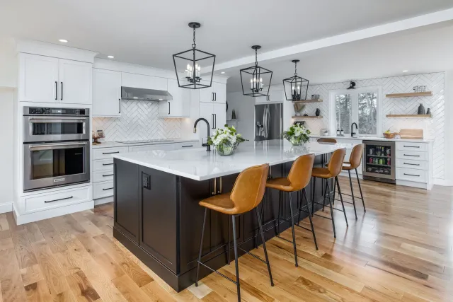 Bright modern kitchen with white cabinets, black island, and three tan barstools on hardwood floors