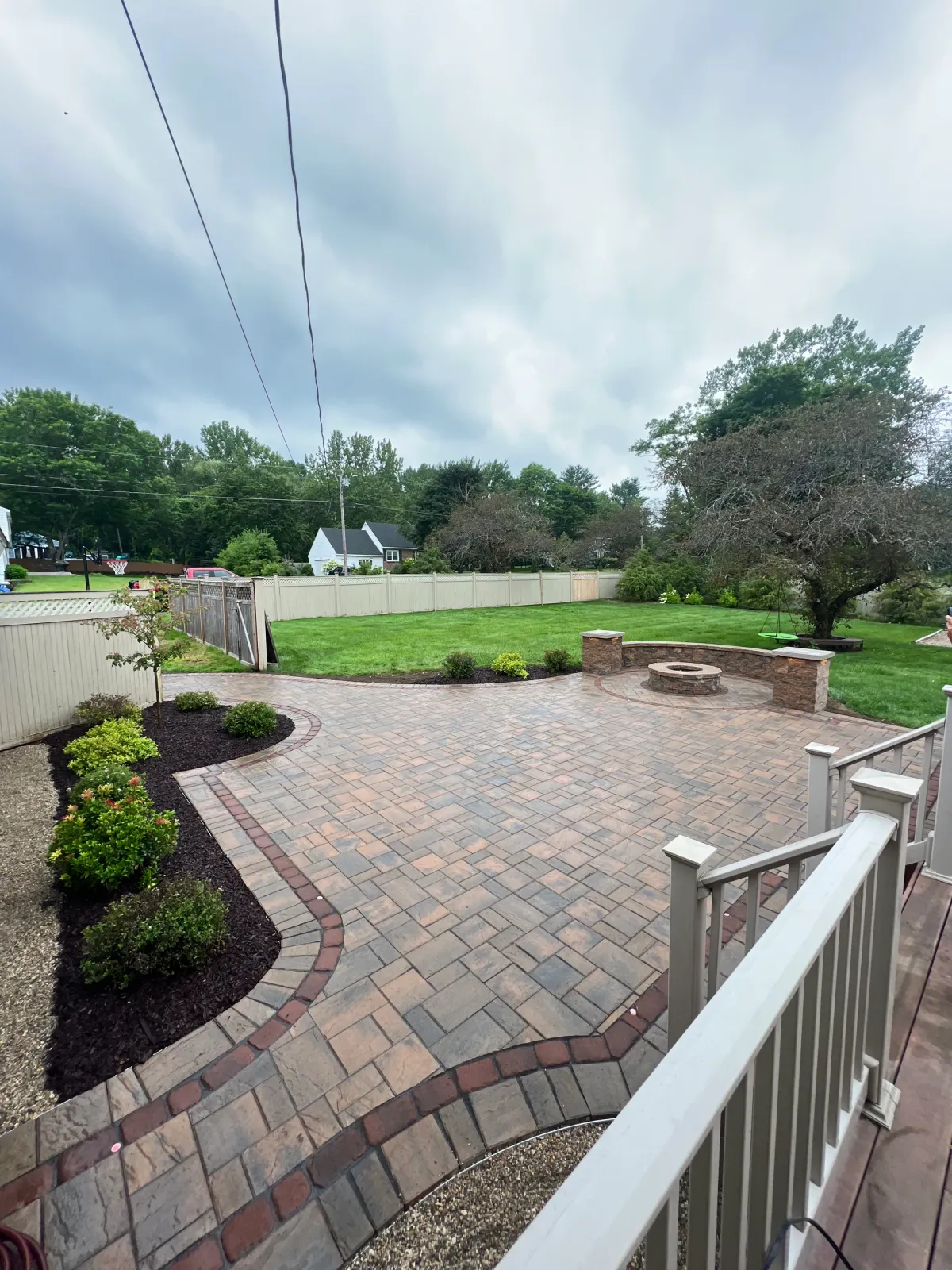 A brick patio with a white railing and a lush green field in the background.