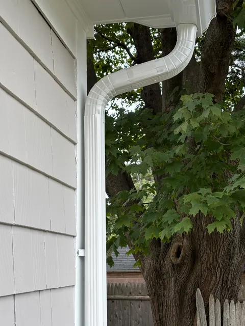 White round downspout with elbow against white painted siding