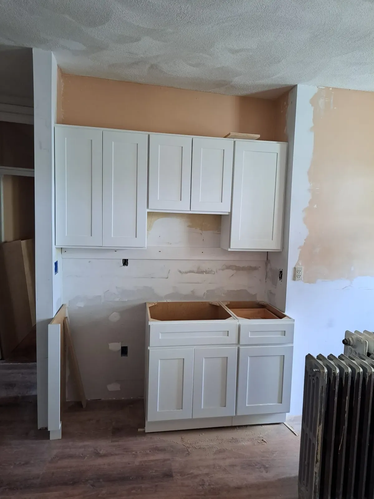 Partially renovated kitchen with white cabinets, exposed wall patches, and a radiator on the right