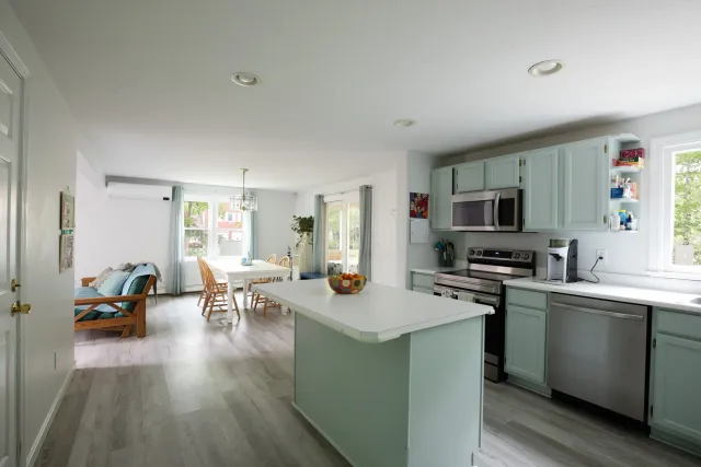 Open-concept kitchen and dining area with light-colored cabinets, stainless steel appliances, and a white countertop kitchen island. Cape Cod Real Estate