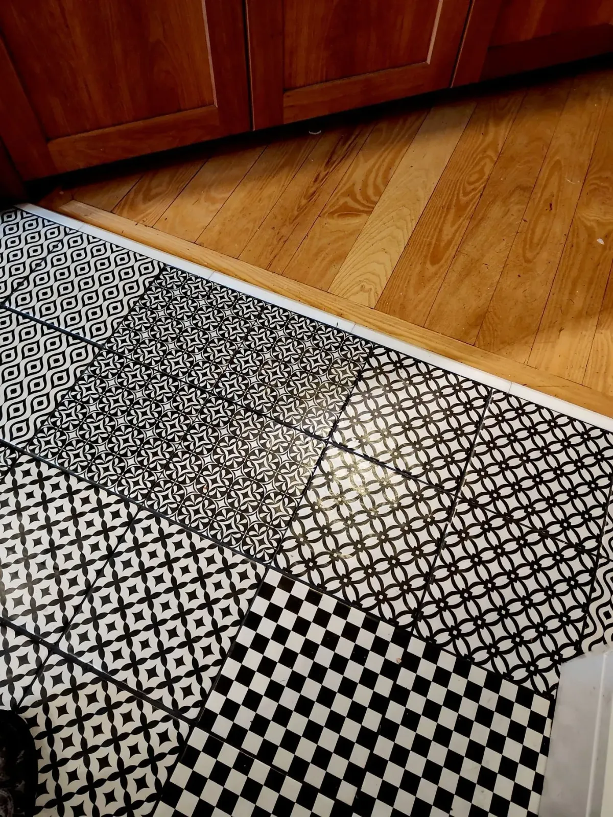 A floor area features decorative black and white patterned tiles bordering light-colored hardwood cabinets.