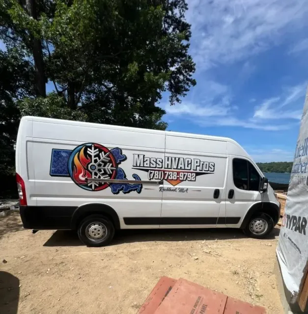 White cargo van with a “MASH VAL VERS” logo parked on a dirt lot under trees and blue sky