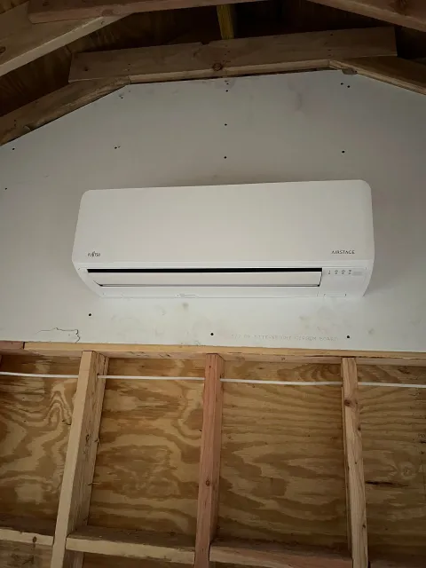 A white air conditioner is hanging from the ceiling of a building under construction.