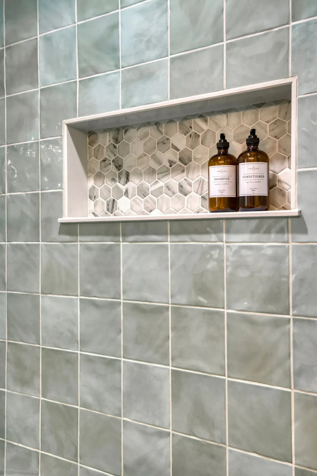 Tiled shower wall with recessed shelf holding two amber soap bottles.