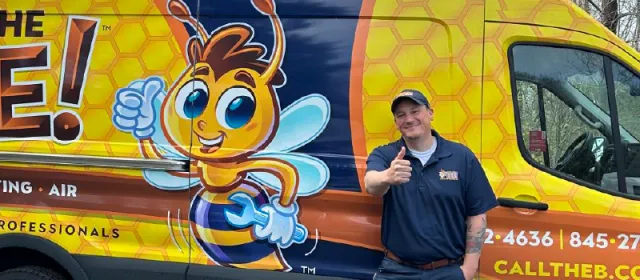 A smiling technician in dark uniform stands beside the bright yellow Call The Bee service van featuring a cartoon bee mascot and contact information.