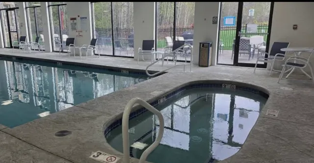Indoor swimming pool and hot tub area with lounge chairs and large windows.