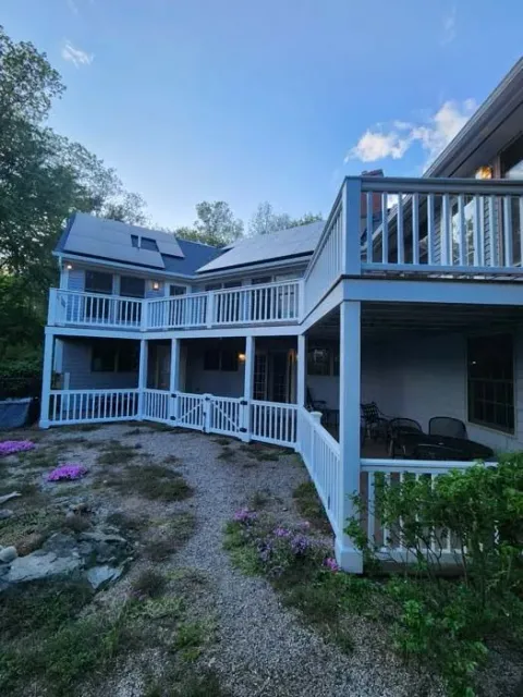 White two-story house with wraparound porch and gravel yard at dusk, viewed from the side