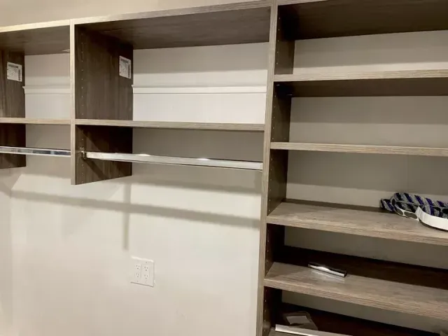 Built-in closet shelving with empty shelves in a beige room, plus a few small items on the right.