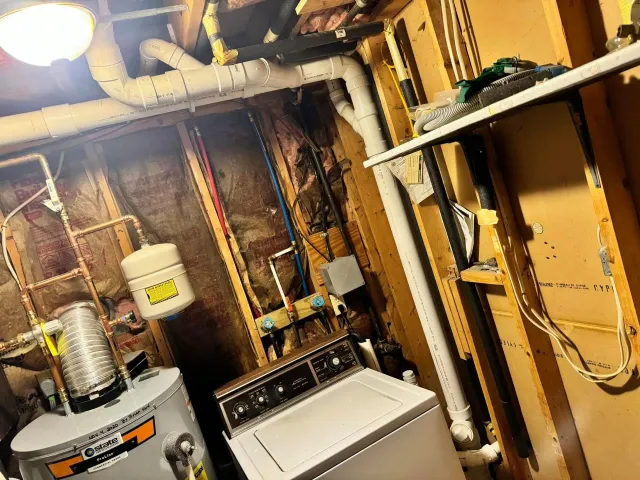 Basement utility area with water heater, washing machine, exposed pipes, and unfinished walls