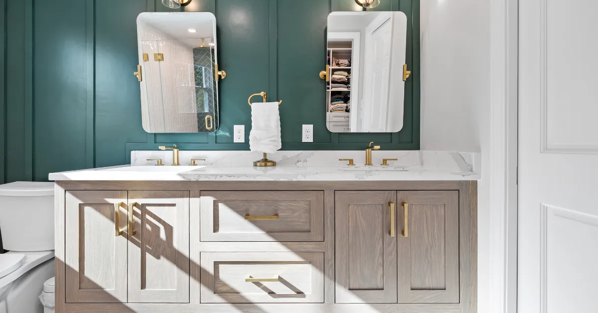 Modern double vanity with gold fixtures, quartz countertop, and green accent wall in a primary bathroom.