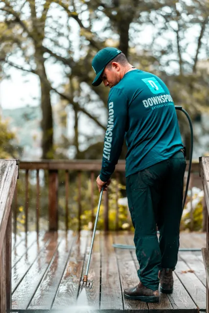 Man in Downspout uniform pressure washing a wooden deck outdoors.