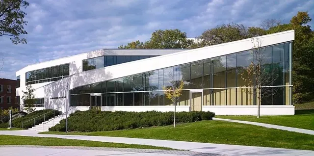 Modern glass-and-white office building with large windows, surrounded by lawn and trees under a blue sky