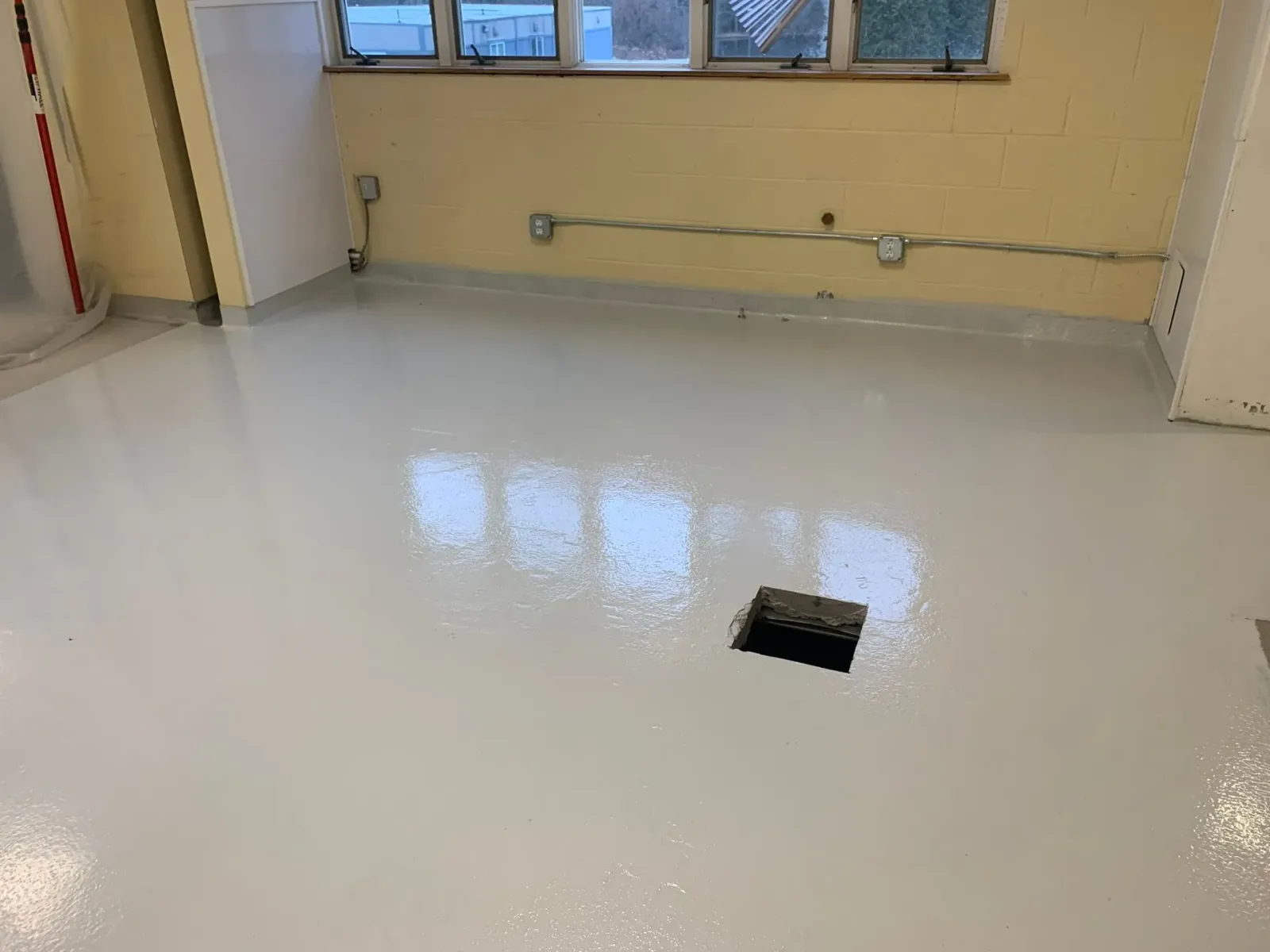 Shiny white floor with a small square opening near a yellow wall and windows.