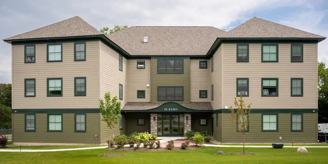 Three-story residential building with green siding and a landscaped front yard.