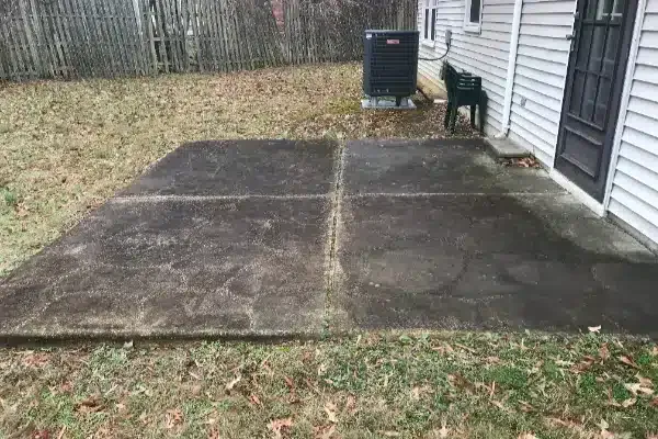 Before: Concrete patio with grass edges, featuring an air conditioning unit and a green chair against a house.