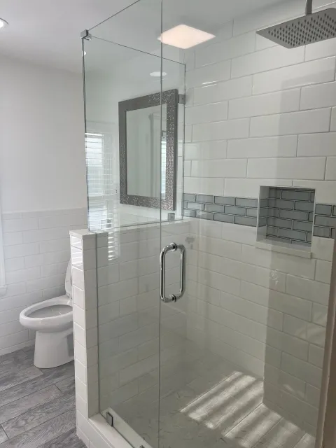 A bathroom with a walk in shower , toilet and mirror.