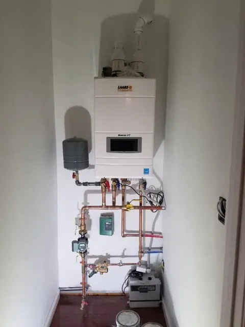 Wall-mounted boiler and exposed plumbing in a narrow utility alcove