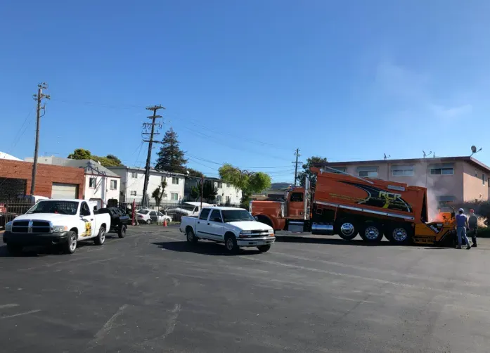Tow truck hauling a red car in a parking lot with two white pickup trucks and workers nearby