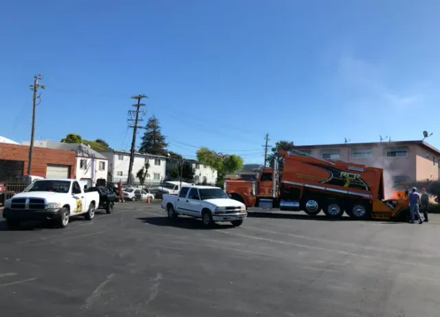 Tow truck hauling a red car in a parking lot with two white pickup trucks and workers nearby