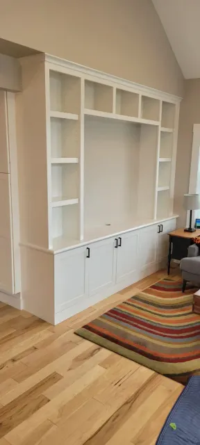 Built-in white wall shelves and cabinets in a bright room with hardwood floors and a striped rug.