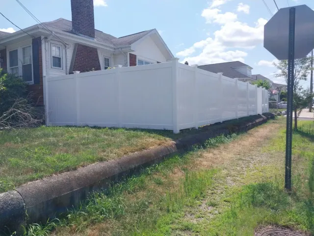 A white fence is surrounding a house on the side of the road.