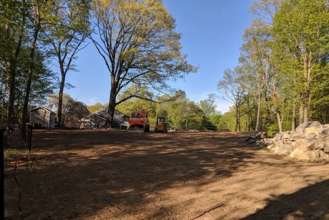 Cleared dirt lot with trees and a red excavator under a clear blue sky
