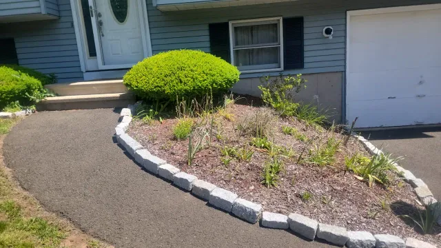 Curved driveway-side planting bed with mixed shrubs and stone edging on a manicured green lawn