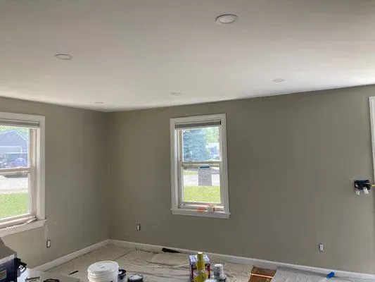 Empty room with olive-green walls, white ceiling, two windows, and recessed lighting.