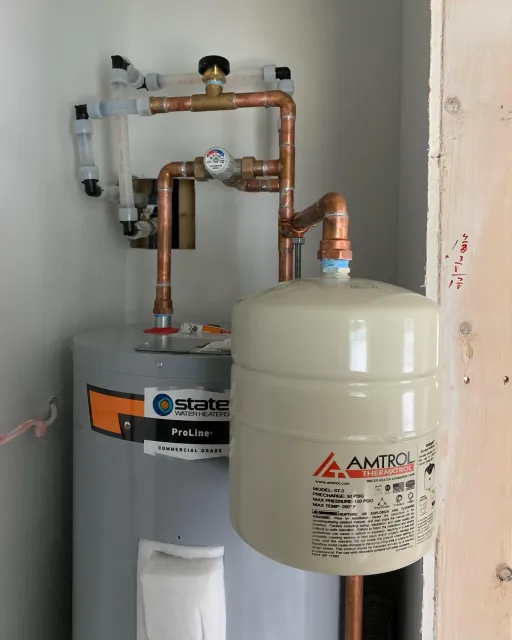 Water heater with connected plumbing and expansion tank in a utility room.